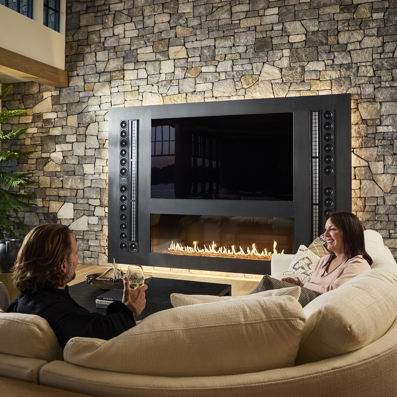 Couple enjoying a glass of wine on the couch in the livingroom with a tv mounted over the fireplace.