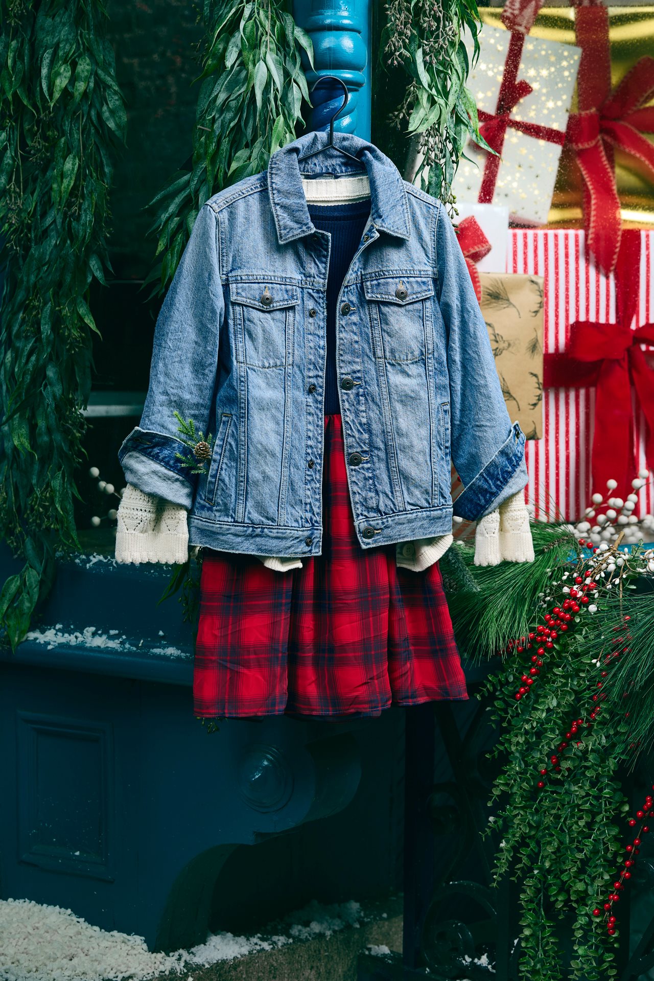 Classic jean jacket completing a layered look outfit on a hanger next to some large wrapped holiday pakages.