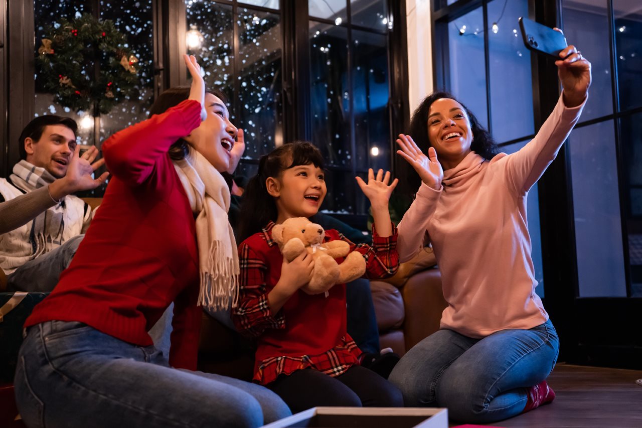 Family at a holiday celebration waving at a cell phone while video chatting family far away.