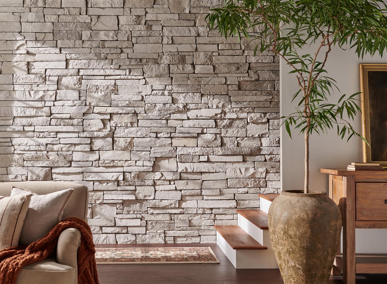 Wheaton Country Ledgestone Cultured Stone as accent wall in a livingroom with rustic furniture and plants.