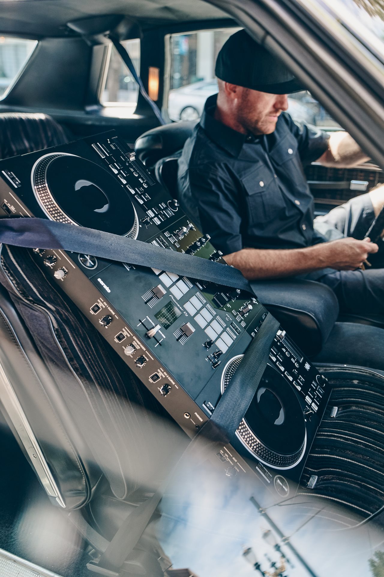 Man in a car with a Pioneer DJ’s DDJ-REV7 seat-belted into the seat next to him.