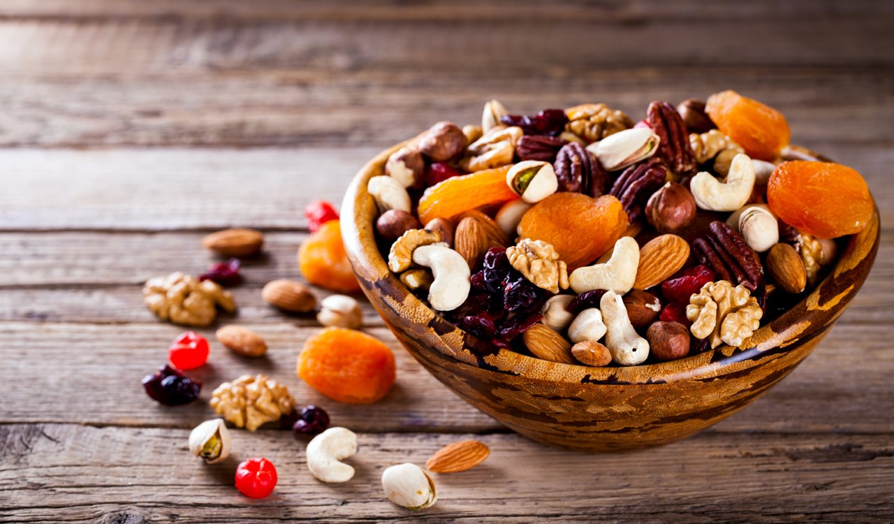 Bowl of fruit and nuts including: Apricots, cashues, cranberries, pecan and walnuts.