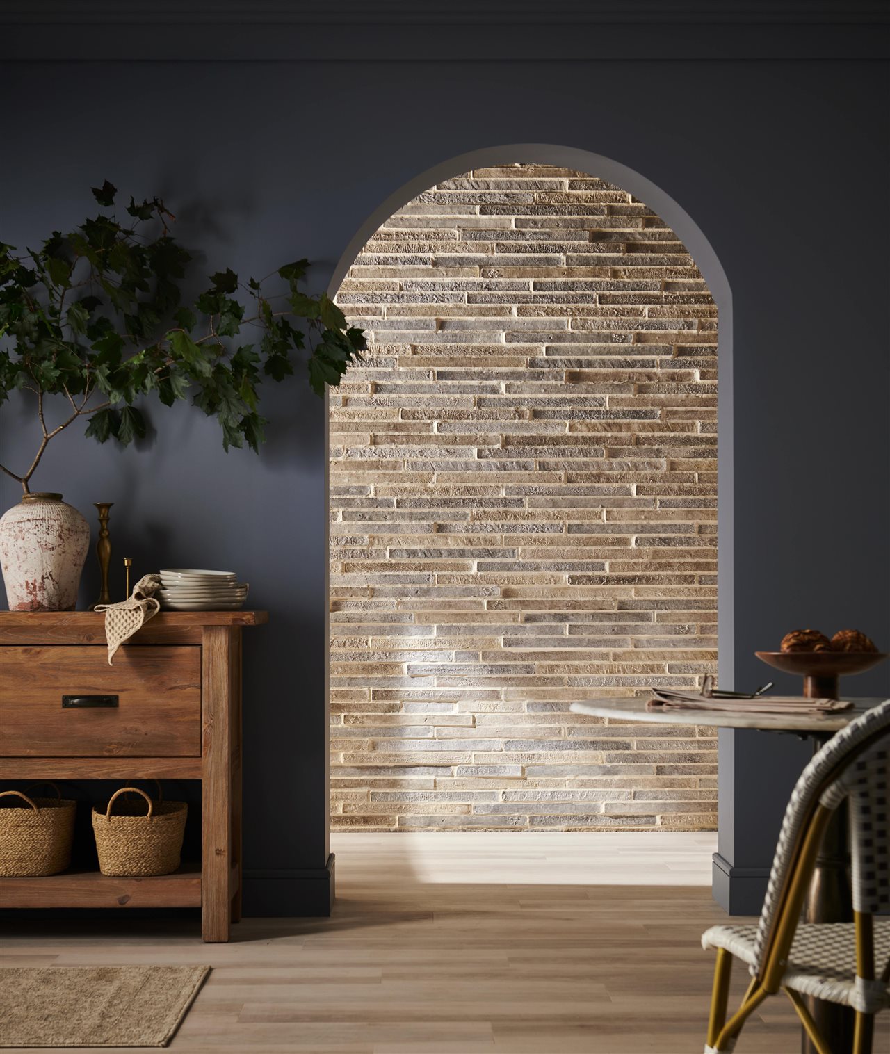 Eledorado stone Loreio Brick wall beyond the archway of a blue room with plants and rustic pots.