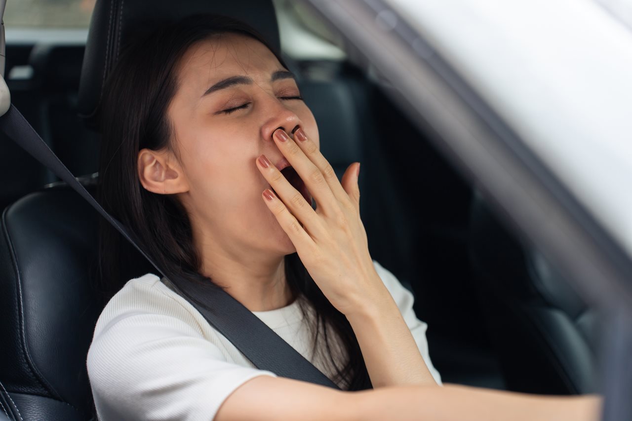 Woman covering a yawn while driving in a car.