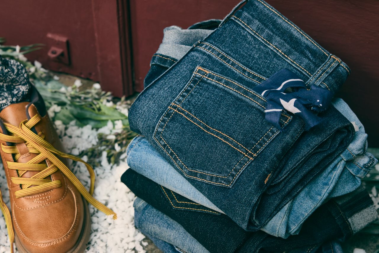 Stack of classic denim jeans next to a pair of hiking boots.