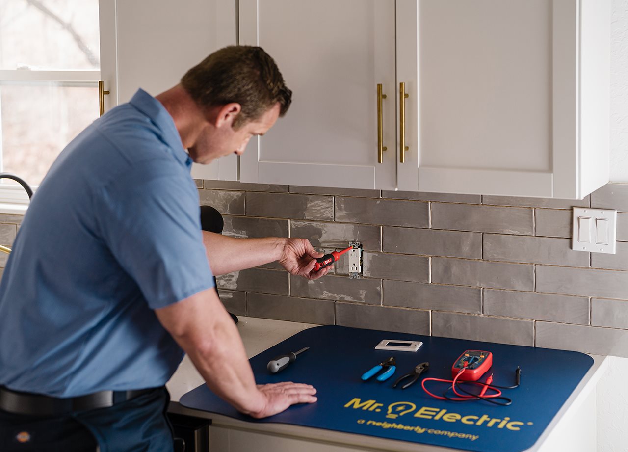 Representative from Mr. Electric working on a electrical box in the kitchen on the back splash near the sink