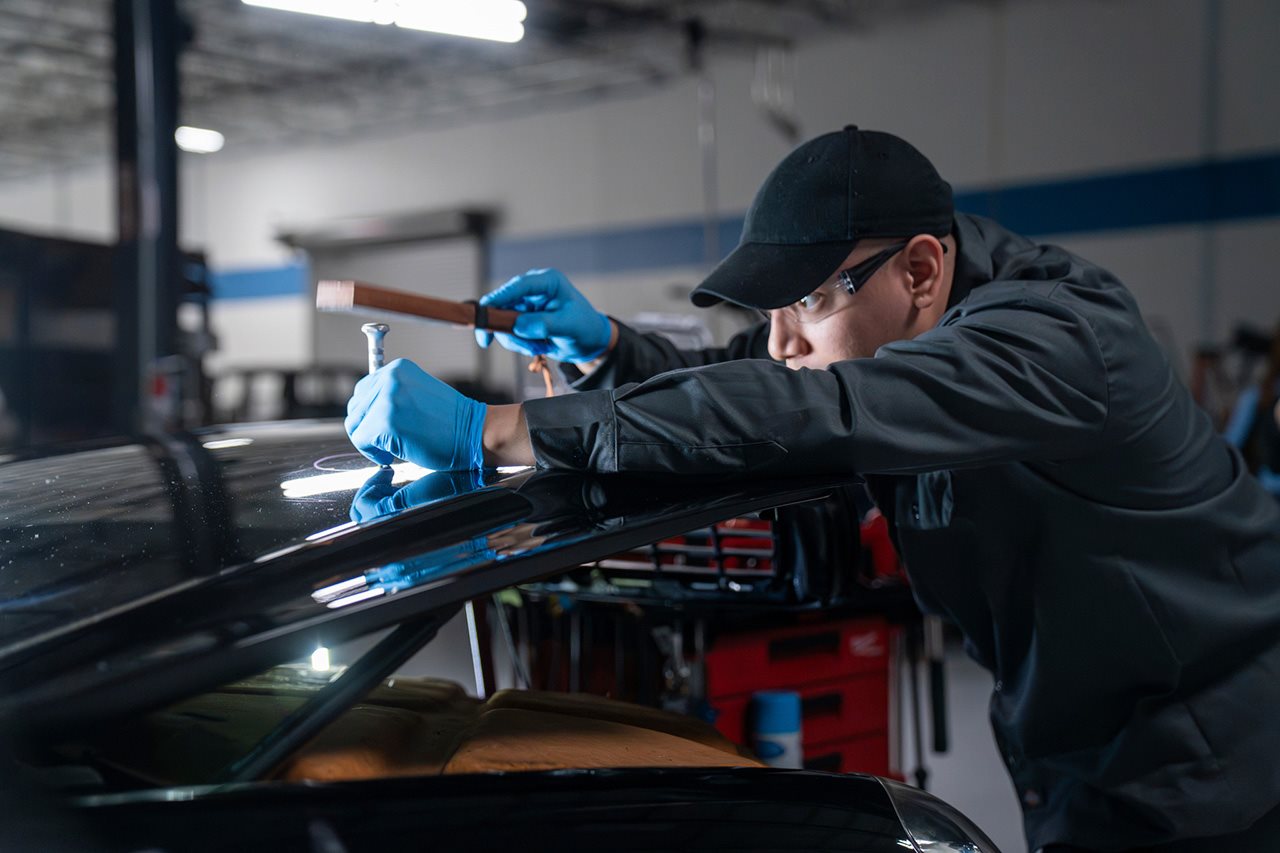 A man taps a tool on the roof of a vehicle.