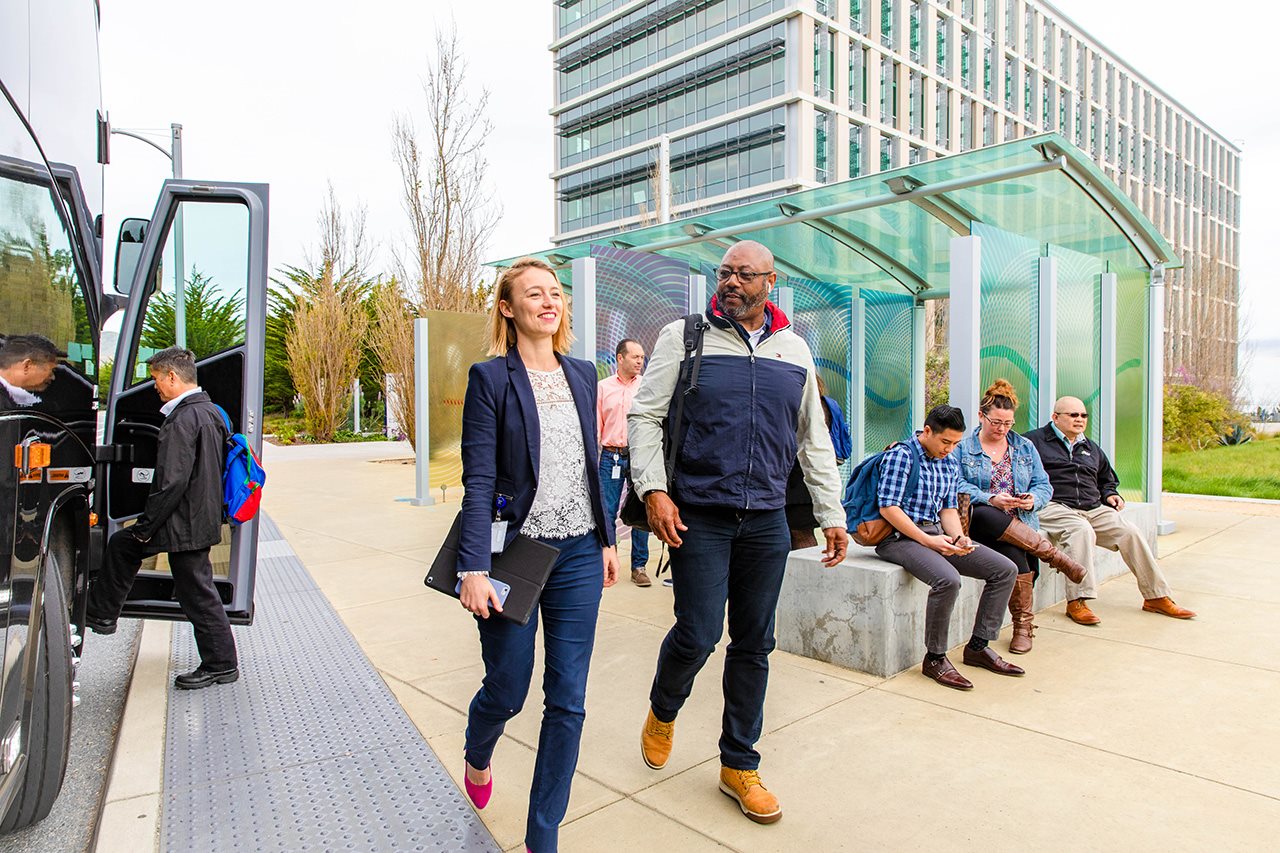 A couple walks and converses as people behind them wait to board a bus.