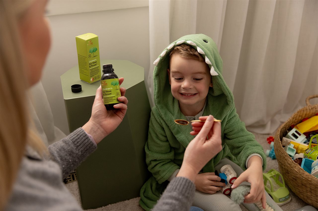 Mother giving little boy in monster costume a spoonful of ear, nose and throat herbal supplement.