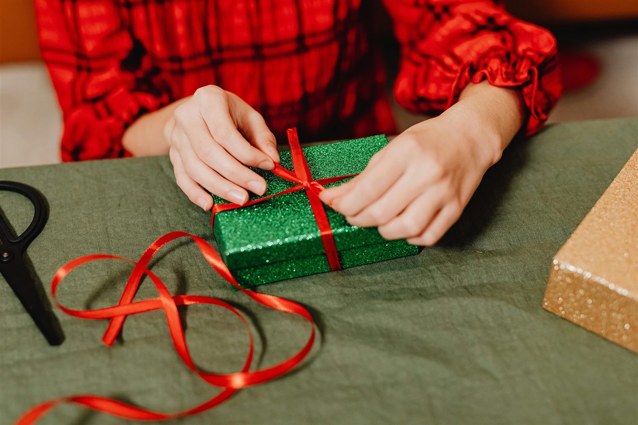 Woman in red plaid shirt wrapping a green and red package for the holidays.