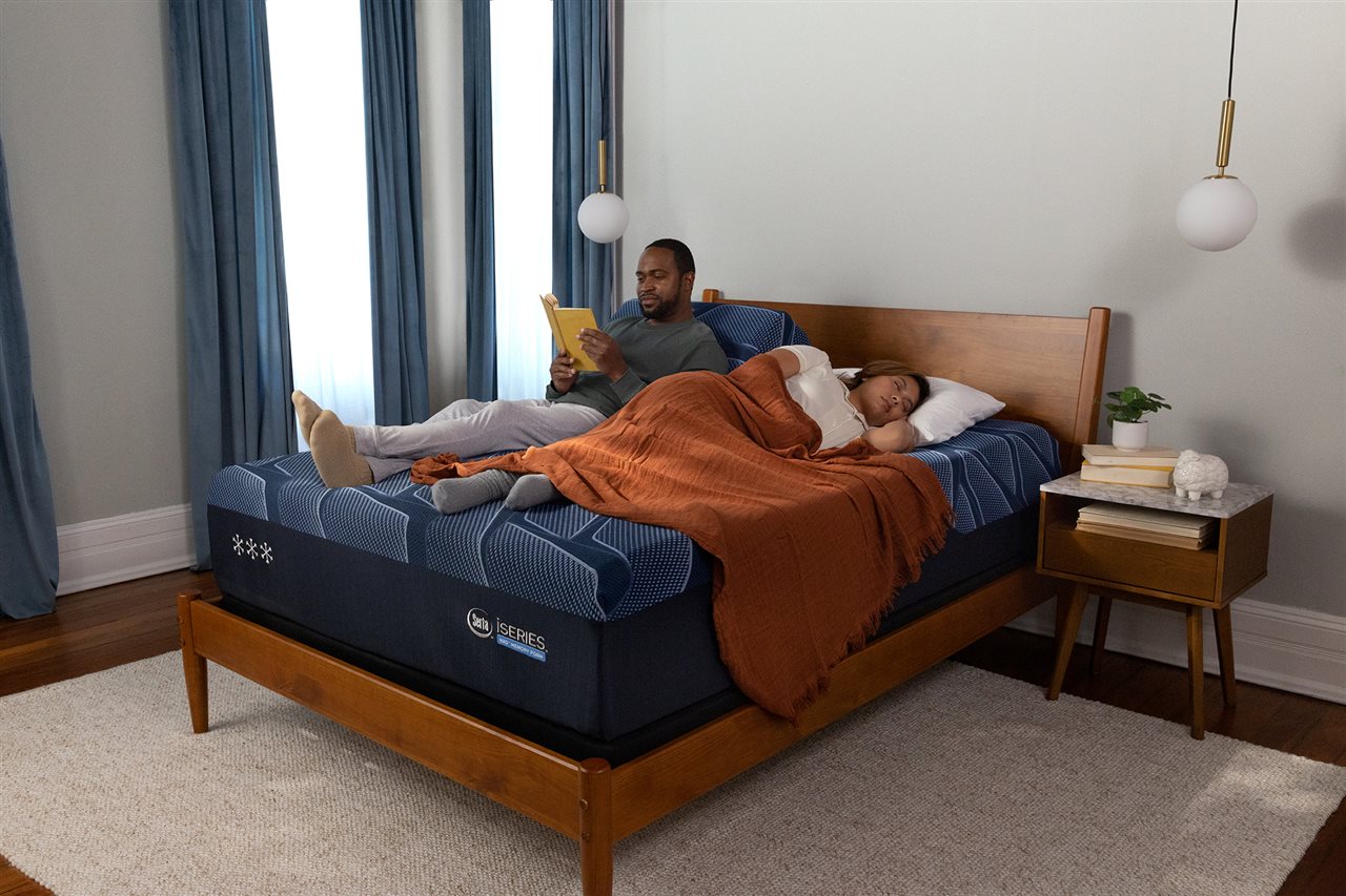 A man reading and a woman sleeping on a Serta's new iSeries NXG™ mattress.