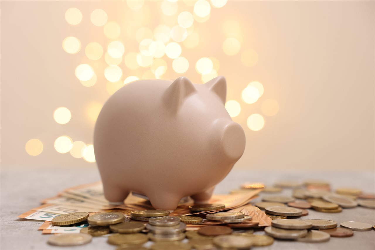 Little pink piggy bank surrounded by coins with a sparkler shinning in the background.