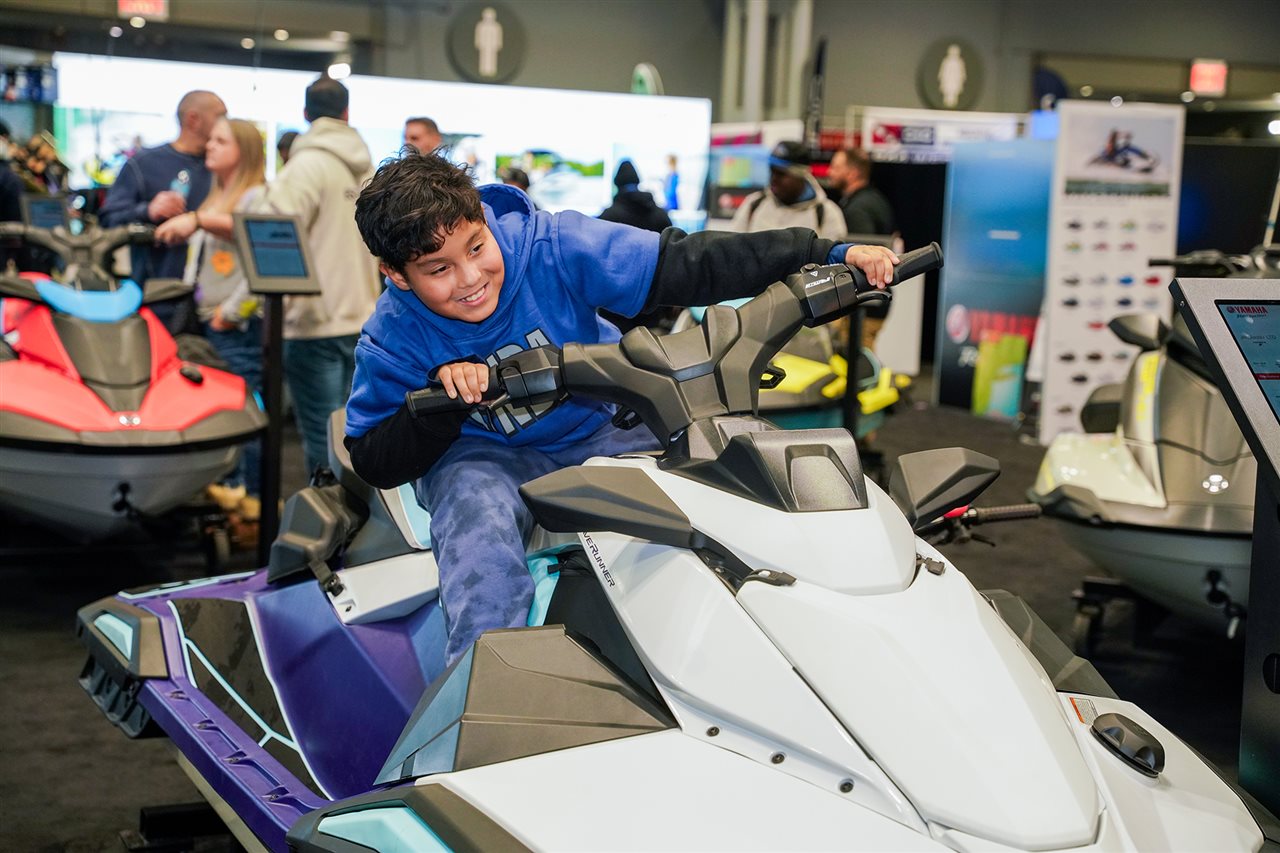 Young man pretending to drive a Jet Ski on the water while at the National Marine Manufacturers Association Boat Show.
