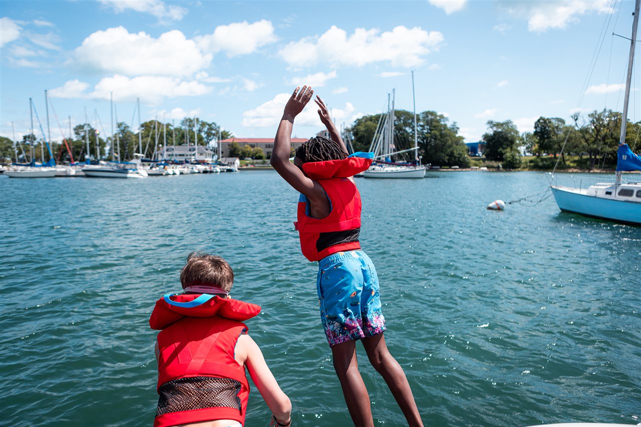 Kids in life jackets jumping off boat. Discover Boating says 