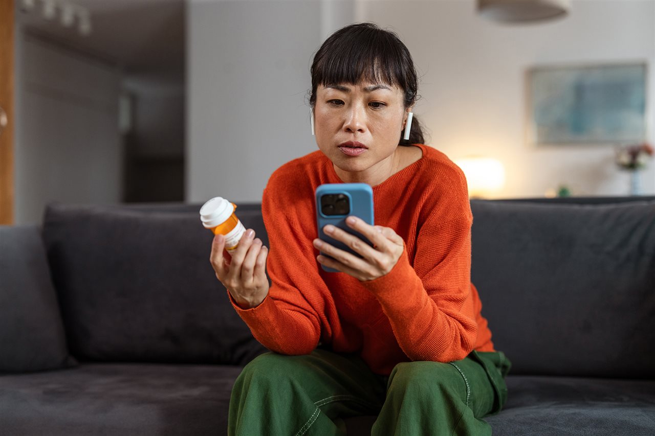 Woman sitting on couch with prescription bottle and using phone phone. BioPlusRX is a specialized pharmacy.