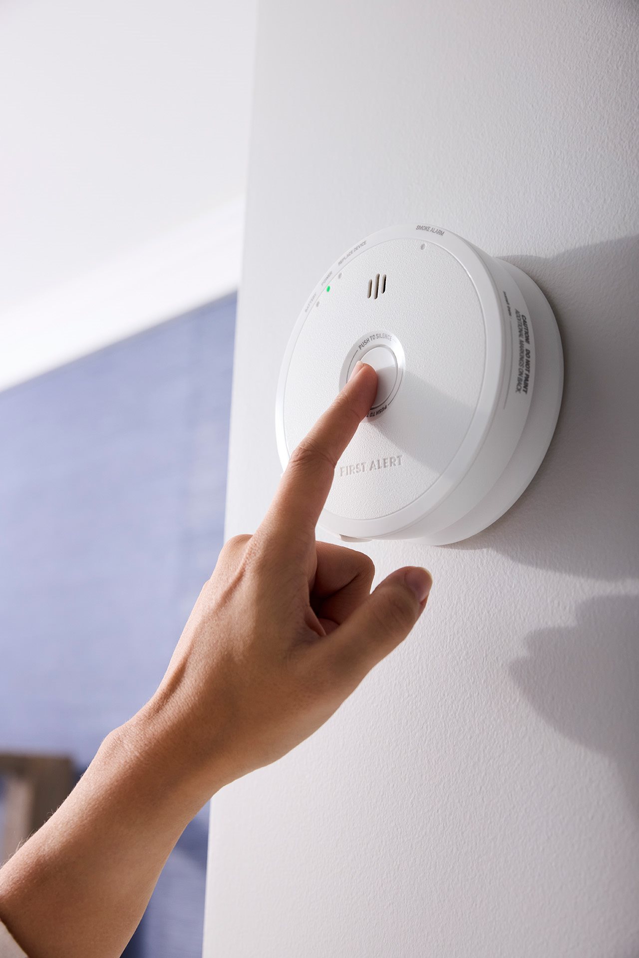 A finger pushes the testing and silence button on a First Alert smoke alarm.