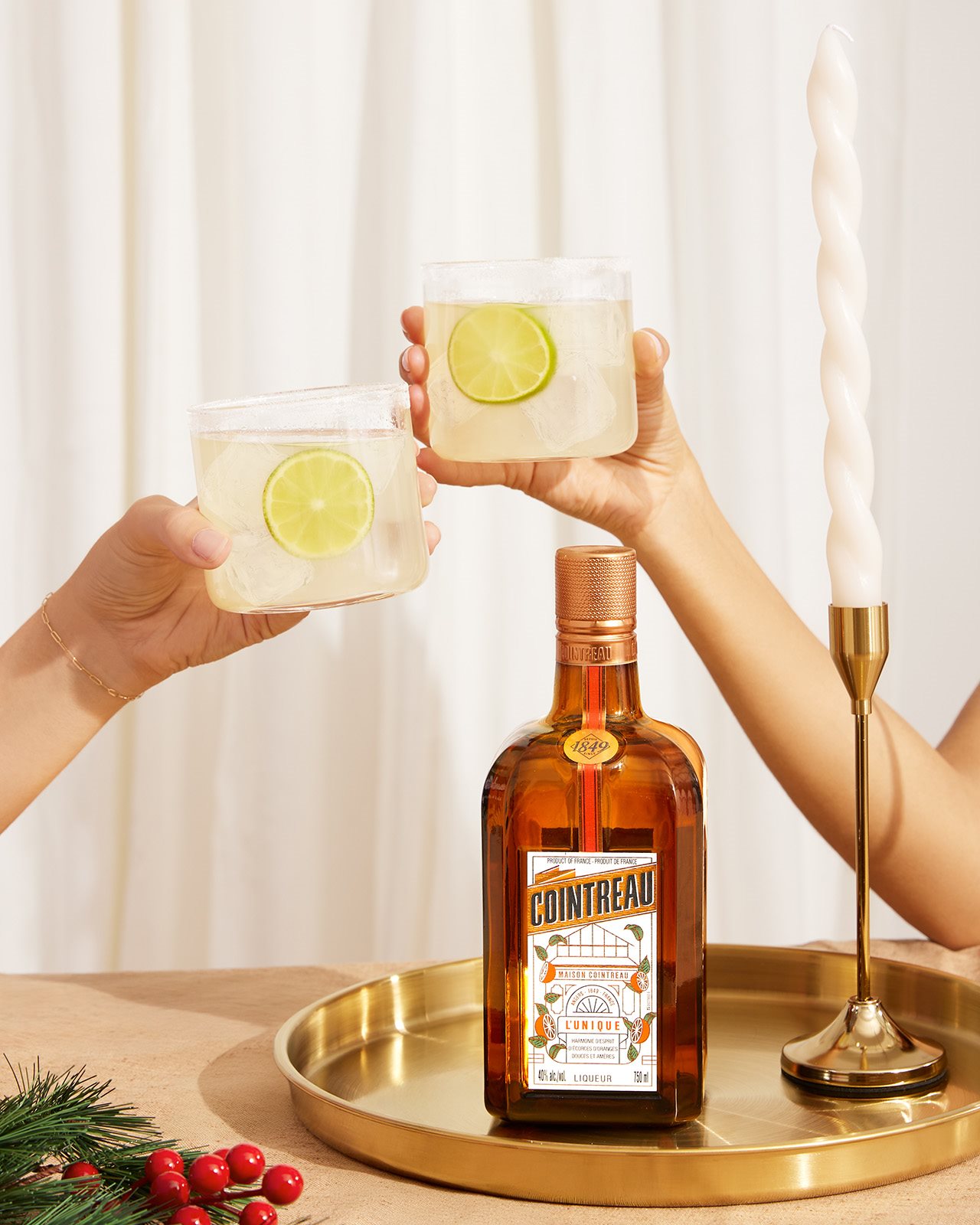 Two people clink their margaritas behind a bottle of Cointreau.